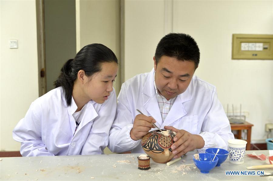 A staff member teaches a girl to repair colored pottery at Gansu Museum in Lanzhou, northwest China\'s Gansu Province, Aug. 16, 2018. The National Cultural Heritage Administration will work out a plan to better protect cultural relics and speed up the creation of a safety oversight platform in 2019. Stressing the importance of such protection, Liu Yuzhu, head of the administration, said lax enforcement is a prominent problem that endangers cultural relics, at a meeting attended by cultural heritage administrators nationwide. (Xinhua/Li Xiao)
