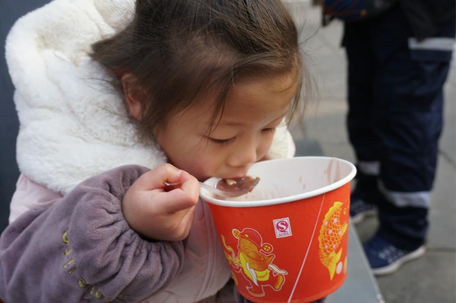 Visitors share Laba congee handed out for free during an event taking place in front of the temple\'s Shaolin Medicine health unit, Jan. 13, 2019. The congee was cooked according to a traditional recipe and included five types of beans as well as more than 20 minor ingredients. Buddhist temples across China have started handing out free Laba congee, a special meal served during the Laba Festival, which falls on the eighth day of the 12th lunar month and ushers in China\'s Lunar New Year celebrations. (Photo: China News Service/Han Zhangyun)