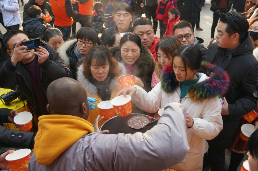 Visitors share Laba congee handed out for free during an event taking place in front of the temple\'s Shaolin Medicine health unit, Jan. 13, 2019. The congee was cooked according to a traditional recipe and included five types of beans as well as more than 20 minor ingredients. Buddhist temples across China have started handing out free Laba congee, a special meal served during the Laba Festival, which falls on the eighth day of the 12th lunar month and ushers in China\'s Lunar New Year celebrations. (Photo: China News Service/Han Zhangyun)