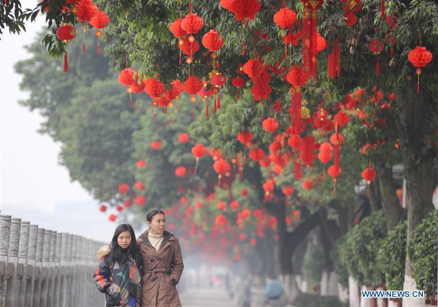 People walk past red decorations on a road in Daoxian County, Yongzhou of central China\'s Hunan Province, Jan. 26, 2019. Red decorations are arranged across China to greet the upcoming lunar New Year which will fall on Feb. 5 this year. (Xinhua/He Hongfu)