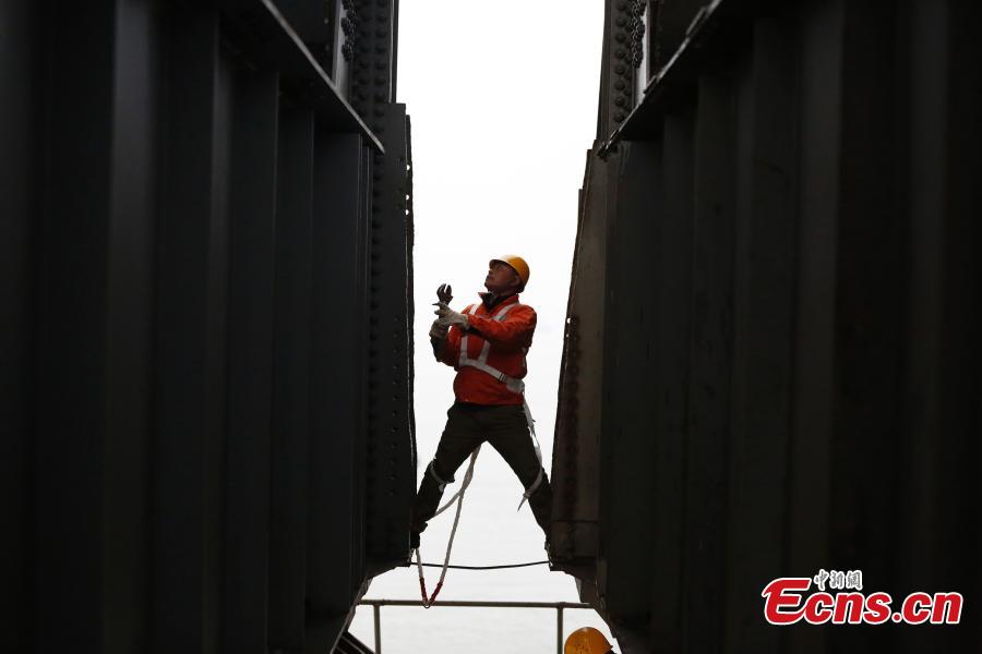 A technician conducts a routine safety check on the Jiujiang Yangtze River Bridge, a major connection of the Beijing-Kowloon Railway in Jiujiang City, East China\'s Jiangxi Province during the travel peak of the Spring Festival. Despite the wind and vibration caused by the passing trains, they continued working in baskets hung under the bridge\'s girder, about 20 meters above the rolling Yangtze River. (Photo: China News Service/Ding Bo)