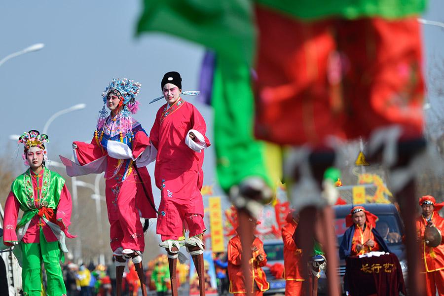 Local performers walk on stilts to celebrate the festival in Zibo, Shandong Province, in March 2018. (PHOTO BY DONG NAIDE/FOR CHINA DAILY)
These days, though, ice lanterns have become larger in size and are often combined with elaborately engraved designs, and the candle has gradually been replaced by a light bulb and, in some cases, even laser lights. The shapes range from small animals, like rabbits, to representations of large structures, such as city walls. The ice engraved lanterns are becoming a folk art all of their own.

Solving lantern riddles is another Lantern Festival tradition. The riddles are written one by one on separate slips of red paper and pasted under the lanterns-the right answer will win a gift for the bright mind who solves the puzzle.

Folk art activities with auspicious meanings, such as lion and dragon dancing, are also part of the celebration of the first full moon of the lunar year. Traditionally, the celebration of Lantern Festival also marks the end of the Spring Festival holiday.