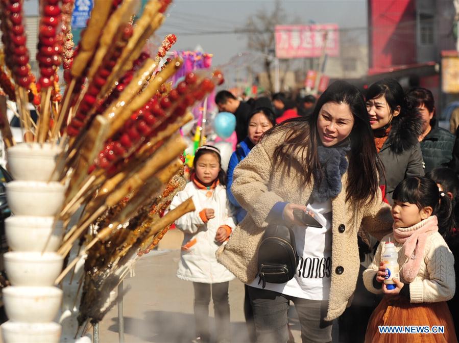 Tourists walk past booths selling tanghulu, a traditional Chinese snack of candied fruit, during an activity to greet the upcoming Lantern Festival in Lihua Village of Renqiu, north China\'s Hebei Province, Feb. 17, 2019. The traditional Chinese Lantern Festival falls on Feb. 19 this year. (Xinhua/Mu Yu)