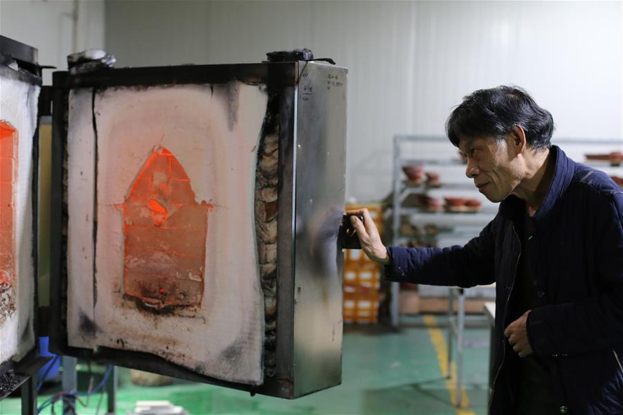 Wu Lizhu, inheritor of the workmanship of Jianzhan teaware, observes pieces of porcelain in the kiln at his workshop in Jianyang District of Nanping City, south China\'s Fujian Province, March 28, 2019. Jianzhan teaware, a well-known Chinese porcelain originated in Jianyang, dates back to more than 1,000 years ago in Song dynasty (960-1279). It was the best teaware for scholars and literati to use during that time in tea competitions. Jianzhan teawares are known for their variability. Glazes can range in color from dark plum to yellow, green, and blue. During the heating and cooling processes, iron element in the clay can migrate within the glaze to form surface crystals in rich and glossy colors, as in the \
