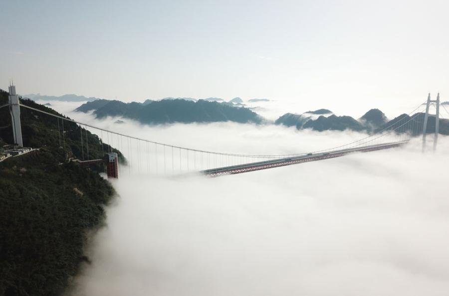 An aerial photo shows the cloudy Aizhai Bridge, a suspension bridge on the Baotou-Maoming Expressway in Jishou city, Hunan Province.  (Photo/chinadaily.com.cn)

Aizhai Bridge, a suspension bridge on the Baotou-Maoming Expressway in Jishou city, Hunan Province, was recently shrouded in a sea of clouds, turning the landscape into a fantasy land as vehicles continued to drive across the bridge. With a main span of 1,176 meters and a deck height of 355 meters, the bridge crosses the Dehang Grand Canyon. It is also the world\'s highest and longest tunnel-to-tunnel bridge.
