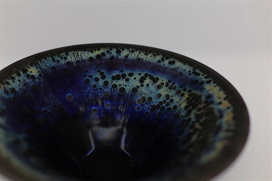 Photo taken on March 28, 2019 shows a piece of porcelain made by Wu Lizhu, inheritor of the workmanship of Jianzhan teaware, at his workshop in Jianyang District of Nanping City, south China\'s Fujian Province. Jianzhan teaware, a well-known Chinese porcelain originated in Jianyang, dates back to more than 1,000 years ago in Song dynasty (960-1279). It was the best teaware for scholars and literati to use during that time in tea competitions. Jianzhan teawares are known for their variability. Glazes can range in color from dark plum to yellow, green, and blue. During the heating and cooling processes, iron element in the clay can migrate within the glaze to form surface crystals in rich and glossy colors, as in the \