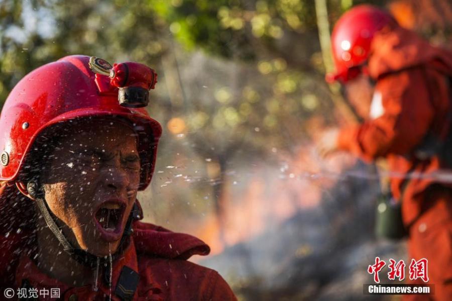 A firefighter suddenly turned back to ask his comrades to spray water on his face to withstand the heat of the fire in southwest China\'s Sichuan Province on March 8, 2015.  (Photo/Agencies)