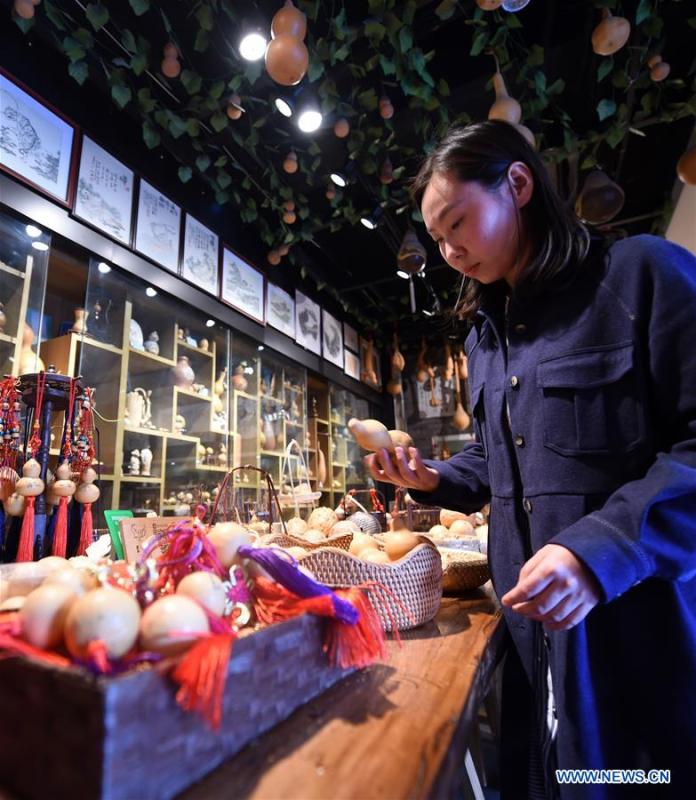 Ruan Xiyue, the fourth generation artist of Carved Gourd Ruan, arranges the handicrafts at a gourd carving studio in Lanzhou, northwest China\'s Gansu Province, April 1, 2019. A carved gourd, as the name suggests, is a gourd carved with landscapes, portraits, animals, calligraphy or poems, and then painted with ink. The process of gourd carving includes choosing gourd, painting, engraving and coloring. It was inscribed in the first group of provincial intangible cultural heritages of Gansu in 2006. (Xinhua/Fan Peishen)