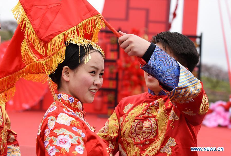 A groom lifts red bridal veil for his bride during a group wedding ceremony in traditional style in Wude Town of Shiqian County, southwest China\'s Guizhou Province, April 4, 2019. A group wedding ceremony in traditional style was held here Thursday for couples who have been striving on the frontline for the county\'s fight against poverty. (Xinhua/Yang Wenbin)