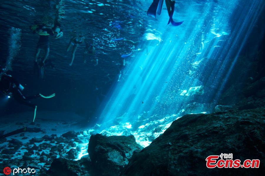 Photo taken by Kirk Zhang shows people diving in freshwater in cenotes illuminated with sunlight from the outside in Mexico. Diving in the caverns, windows to large underground river systems, is a unique experience with  amazing light effects. (Photo/IC)
