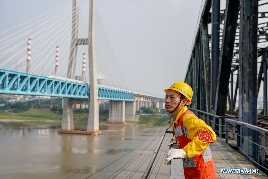 Tang Jinhua looks at the new Baishatuo Yangtze River railway bridge in Jiangjin of southwest China\'s Chongqing Municipality, April 23, 2019. The previous Baishatuo Yangtze River railway bridge, completed in 1959, will stop service after April 24. All trains will run on the new double decker steel truss cable stay railway bridge after that day. The new bridge has 4 tracks on the upper deck for passenger trains with a designed speed of 200 kilometers per hour and 2 tracks on the lower deck for cargo trains with the designed speed of 120 kilometers per hour. (Xinhua/Liu Chan)