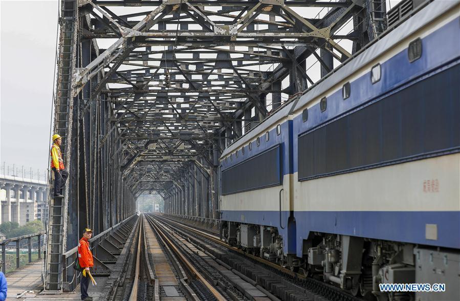 Workers wait for an electrical locomotive to pass on the previous Baishatuo Yangtze River railway bridge in Jiangjin of southwest China\'s Chongqing Municipality, April 23, 2019. The previous Baishatuo Yangtze River railway bridge, completed in 1959, will stop service after April 24. All trains will run on the new double decker steel truss cable stay railway bridge after that day. The new bridge has 4 tracks on the upper deck for passenger trains with a designed speed of 200 kilometers per hour and 2 tracks on the lower deck for cargo trains with the designed speed of 120 kilometers per hour. (Xinhua/Liu Chan)