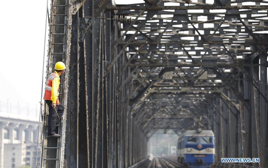 A worker waits for an electrical locomotive to pass on the previous Baishatuo Yangtze River railway bridge in Jiangjin of southwest China\'s Chongqing Municipality, April 23, 2019. The previous Baishatuo Yangtze River railway bridge, completed in 1959, will stop service after April 24. All trains will run on the new double decker steel truss cable stay railway bridge after that day. The new bridge has 4 tracks on the upper deck for passenger trains with a designed speed of 200 kilometers per hour and 2 tracks on the lower deck for cargo trains with the designed speed of 120 kilometers per hour. (Xinhua/Liu Chan)