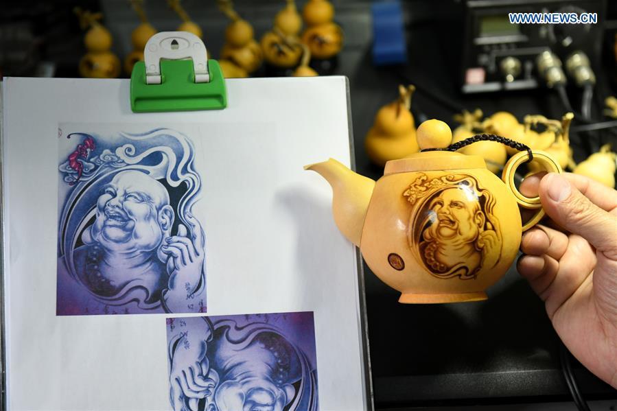 Craftsman Liu Chunpu compares the cucurbits pyrography work with a design drawing at a studio in Yuhua District of Shijiazhuang, north China\'s Hebei Province, April 23, 2019. Liu Chunpu, a staff member of Hebei Normal University, has devoted himself in cucurbit pyrography for more than 40 years. (Xinhua/Xu Jianyuan)