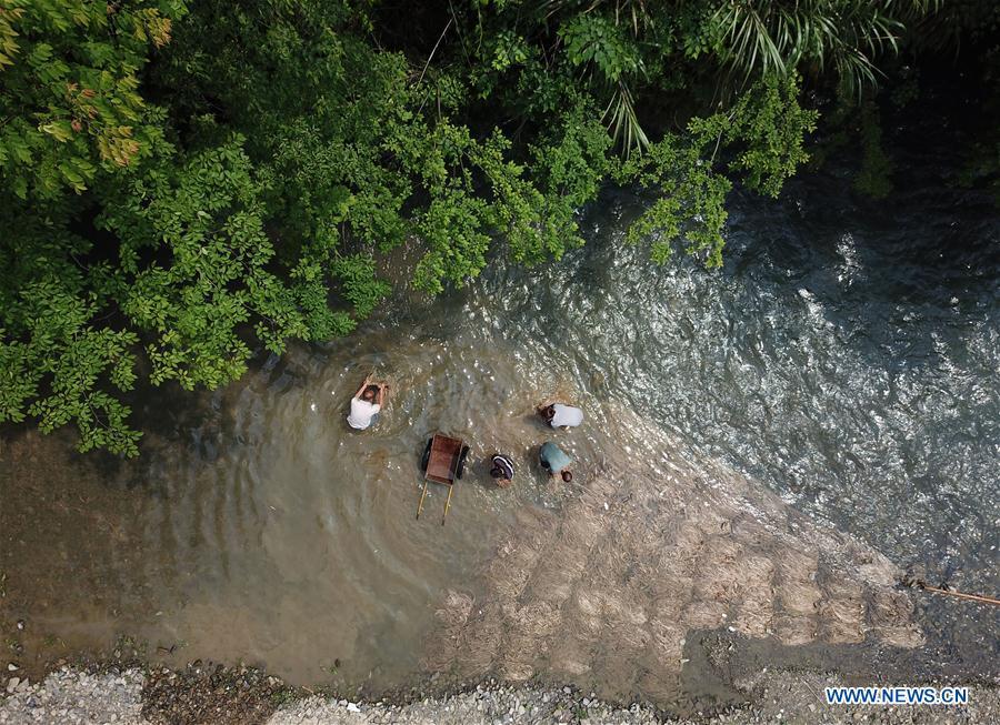 Aerial photo shows craftsmen washing raw materials in a river in Shiqiao Village of Danzhai County, southwest China\'s Guizhou Province, April 24, 2019. Wang Xingwu, 53, a national intangible cultural heritage inheritor in papermaking, learned the papermaking technique from his family as a child. Besides exerting the old papermaking technique to its full potential, Wang keeps raising product quality and improving the making procedure. With the involvement of plants in the papermaking process, he has created more than 160 kinds of patterned papers and paper crafts. He also develops a kind of handmade white paper more suitable for writing calligraphy and painting. (Xinhua/Huang Xiaohai)