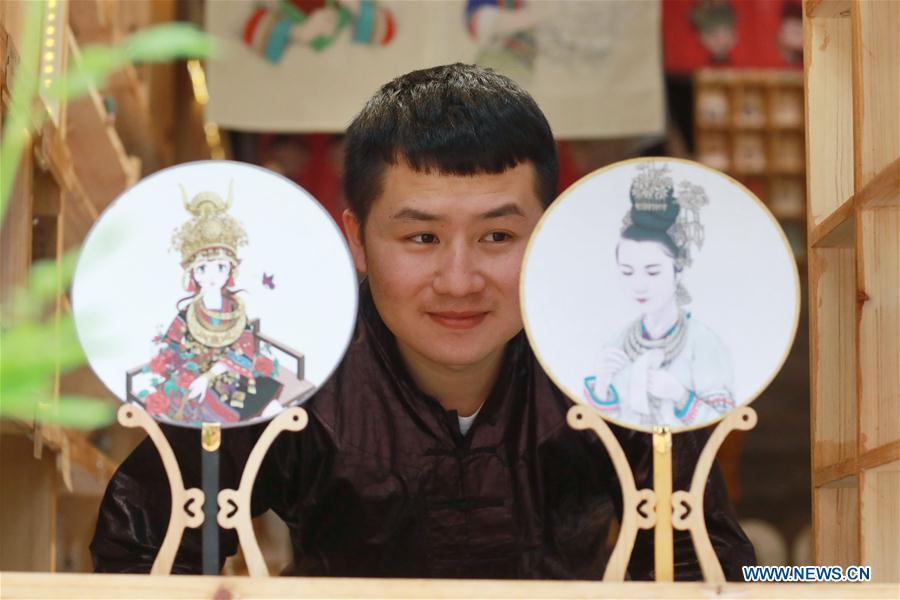 Lan Caisheng, an illustrator born in the 1990s, views fans with his illustrations as coverings at his own studio in Liping County, southwest China\'s Guizhou Province, April 16, 2019. After graduation in 2015, Lan returned to his hometown in Liping County and started a studio to make illustrations and related products featuring ethnic minority cultures including the Miao and Dong ethnic groups. His illustrations are widely known in Liping and recognized by tourists at home and abroad. Lan wishes, through illustrations he made, ethnic minority cultures in Guizhou could reach more people in the future. A nation will prosper only when its young people thrive; a country will be full of hope and have a great tomorrow only when its younger generations have ideals, ability, and a strong sense of responsibility. Young people always play a vanguard role in realizing national rejuvenation, which is the mission of the Chinese youth in the new era. In China many young people realize the value of life through hard work. They are writing a brilliant chapter worthy of our times in their efforts to take advantage of their youthful vigor, explore life and contribute to society. (Xinhua/Ou Dongqu)