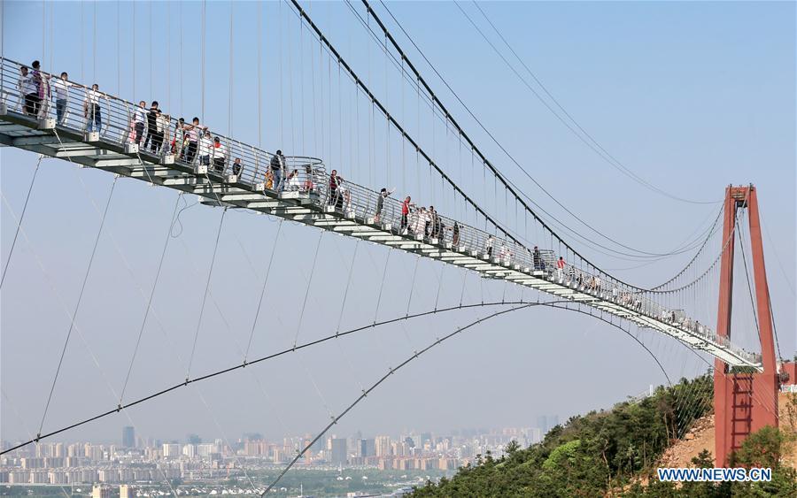 Tourists walk on a glass bridge at the Huaxi World Adventure Park in Huaxi Village of Jiangyin City, east China\'s Jiangsu Province, May 4, 2019. The 518-meter-long glass bridge hangs more than 100 meters above ground level at the park. It is made of panes of 35-mm-thick glass. Each glass can hold a maximum weight of 4.7 tonnes. Around 2,600 people can cross the bridge at a time. (Xinhua/Xu Congjun)