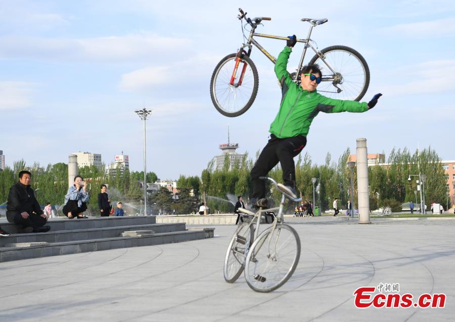 Zhou Changchun, 59, shows off his cycling stunts at a square in Changchun City, Northeast China\'s Jilin Province, May 7, 2019. Zhou is able to perform a number of stunts while riding his bicycle, including standing and lifting dumbbells with both hands. (Photo: China News Service/Zhang Yao)