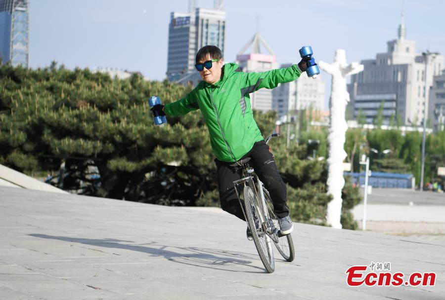 Zhou Changchun, 59, shows off his cycling stunts at a square in Changchun City, Northeast China\'s Jilin Province, May 7, 2019. Zhou is able to perform a number of stunts while riding his bicycle, including standing and lifting dumbbells with both hands. (Photo: China News Service/Zhang Yao)