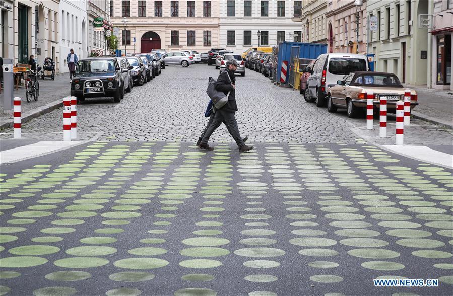 Two pedestrians walk across a green dotted street area in Bergmann Street of Kreuzberg, southern Berlin, Germany, on May 7, 2019. The green dots, part of new street signals in Berlin, are applied as a trial at a part of Bergmann Street with a speed limit of 20km/h, aiming to induce vehicles to drive with restricted speed. (Xinhua/Shan Yuqi)