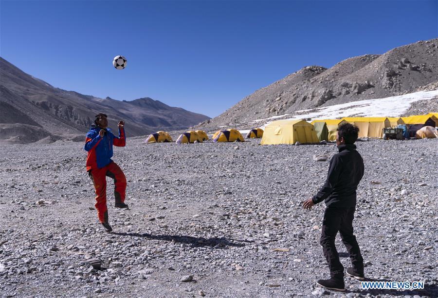 The mountain guide Zhaxi Dondrup plays football at the base camp of the northern face of Mount Qomolangma in southwest China\'s Tibet Autonomous Region, April 26, 2019. Every year, for a few weeks, hundreds of climbers and supporting personnel come to the base camp of the northern face of Mount Qomolangma, trying to reach the summit of the tallest and most famous mountain in the world. Before starting climbing, they need to hike several times between elevations from 5,000 meters to 7,000 meters, giving their bodies some time to adapt. When this process is over, it\'s all up to the weather. The base camp is a popular place to wait for the window. Among the six camps on the northern face, the base camp at an altitude of 5,200 meters is the furthest cars can reach and therefor the most equipped. Besides food and accommodation, climbers can also enjoy tea and massage. They can also play football on perhaps the highest field. There\'s even a simple gym in the camp. Environmental protection is a priority here. Garbage sacks are given to each climbing team. Special containers are put in every camp to collect trash and sewage. The collected trash must be treated 100 kilometers away, and the only road is a zigzagging track. It is not trucks, but yaks that are generally used to make the journey. Actually yaks are vital on the mountain. Beyond the base camp, yak is the only reliable transport. (Xinhua/Sun Fei)