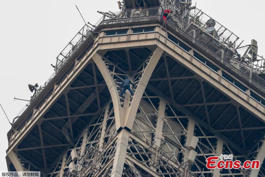 A man (C) climbs up to the top of the Eiffel Tower, in Paris, without any protection as a firefighter (R) looks down at him from the top, on May 20, 2019. The Eiffel Tower was evacuated on May 20, 2019 in the afternoon after a person was spotted climbing up the Paris landmark, the company that operates the structure said. \