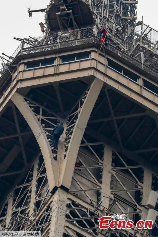 A man (C) climbs up to the top of the Eiffel Tower, in Paris, without any protection as a firefighter (R) looks down at him from the top, on May 20, 2019. The Eiffel Tower was evacuated on May 20, 2019 in the afternoon after a person was spotted climbing up the Paris landmark, the company that operates the structure said. \