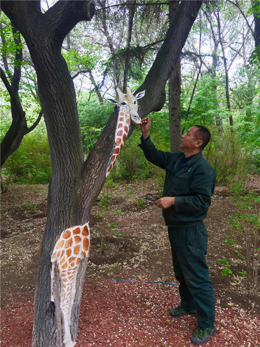 Feng Shuxuan paints a giraffe on a tree trunk in the Zoological and Botanical Garden in Changchun. (Photo/chinadaily.com.cn)