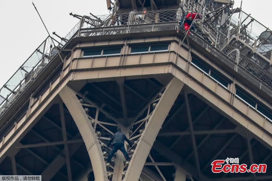 A man (C) climbs up to the top of the Eiffel Tower, in Paris, without any protection as a firefighter (R) looks down at him from the top, on May 20, 2019. The Eiffel Tower was evacuated on May 20, 2019 in the afternoon after a person was spotted climbing up the Paris landmark, the company that operates the structure said. \