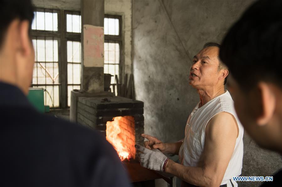 Zheng Guorong teaches skills of sword making to his apprentices at Guyue Sword Studio in Longquan, east China\'s Zhejiang Province, May 21, 2019. For centuries, Longquan has been famed for its sword making industry. Zheng Guorong, 55, an intangible cultural heritage inheritor in Longquan Sword making, has been making sword for more than 30 years. Zheng regards sword as a symbol of spirit and devotes all to his career with awe. In his studio, the whole process of making a single sword takes two to three months, with steps including forming an idea, designing the sketch, preparing material and the final making and assembling. After setting up his studio, Zheng has trained more than 20 apprentices, who have all become sword smiths of great reputation. The old sword smith insists that Longquan sword, with a history of more than 2,500 years, deserves to be carried on in our time, both materially and spiritually. (Xinhua/Weng Xinyang)