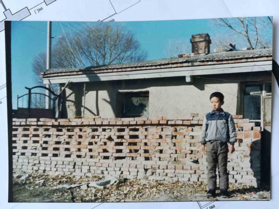 An old photo shows Wang Tao standing in front of the rammed-earth house he lived in as a child. (Photo provided to chinadaily.com.cn)