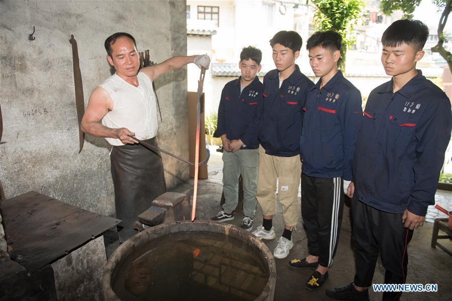 Zheng Guorong (L) teaches skills of sword making to his apprentices at Guyue Sword Studio in Longquan, east China\'s Zhejiang Province, May 21, 2019. For centuries, Longquan has been famed for its sword making industry. Zheng Guorong, 55, an intangible cultural heritage inheritor in Longquan Sword making, has been making sword for more than 30 years. Zheng regards sword as a symbol of spirit and devotes all to his career with awe. In his studio, the whole process of making a single sword takes two to three months, with steps including forming an idea, designing the sketch, preparing material and the final making and assembling. After setting up his studio, Zheng has trained more than 20 apprentices, who have all become sword smiths of great reputation. The old sword smith insists that Longquan sword, with a history of more than 2,500 years, deserves to be carried on in our time, both materially and spiritually. (Xinhua/Weng Xinyang)