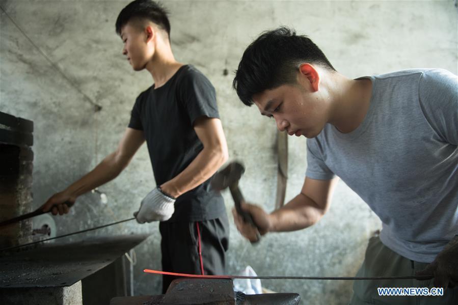 Apprentices of Zheng Guorong practice sword making at Guyue Sword Studio in Longquan, east China\'s Zhejiang Province, May 21, 2019. For centuries, Longquan has been famed for its sword making industry. Zheng Guorong, 55, an intangible cultural heritage inheritor in Longquan Sword making, has been making sword for more than 30 years. Zheng regards sword as a symbol of spirit and devotes all to his career with awe. In his studio, the whole process of making a single sword takes two to three months, with steps including forming an idea, designing the sketch, preparing material and the final making and assembling. After setting up his studio, Zheng has trained more than 20 apprentices, who have all become sword smiths of great reputation. The old sword smith insists that Longquan sword, with a history of more than 2,500 years, deserves to be carried on in our time, both materially and spiritually. (Xinhua/Weng Xinyang)