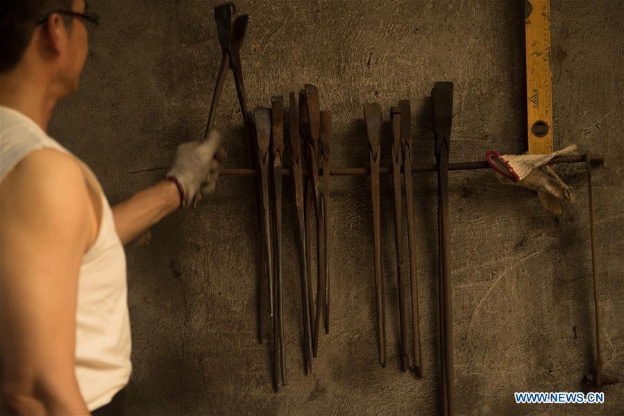 Zheng Guorong works at Guyue Sword Studio in Longquan, east China\'s Zhejiang Province, May 21, 2019. For centuries, Longquan has been famed for its sword making industry. Zheng Guorong, 55, an intangible cultural heritage inheritor in Longquan Sword making, has been making sword for more than 30 years. Zheng regards sword as a symbol of spirit and devotes all to his career with awe. In his studio, the whole process of making a single sword takes two to three months, with steps including forming an idea, designing the sketch, preparing material and the final making and assembling. After setting up his studio, Zheng has trained more than 20 apprentices, who have all become sword smiths of great reputation. The old sword smith insists that Longquan sword, with a history of more than 2,500 years, deserves to be carried on in our time, both materially and spiritually. (Xinhua/Weng Xinyang)