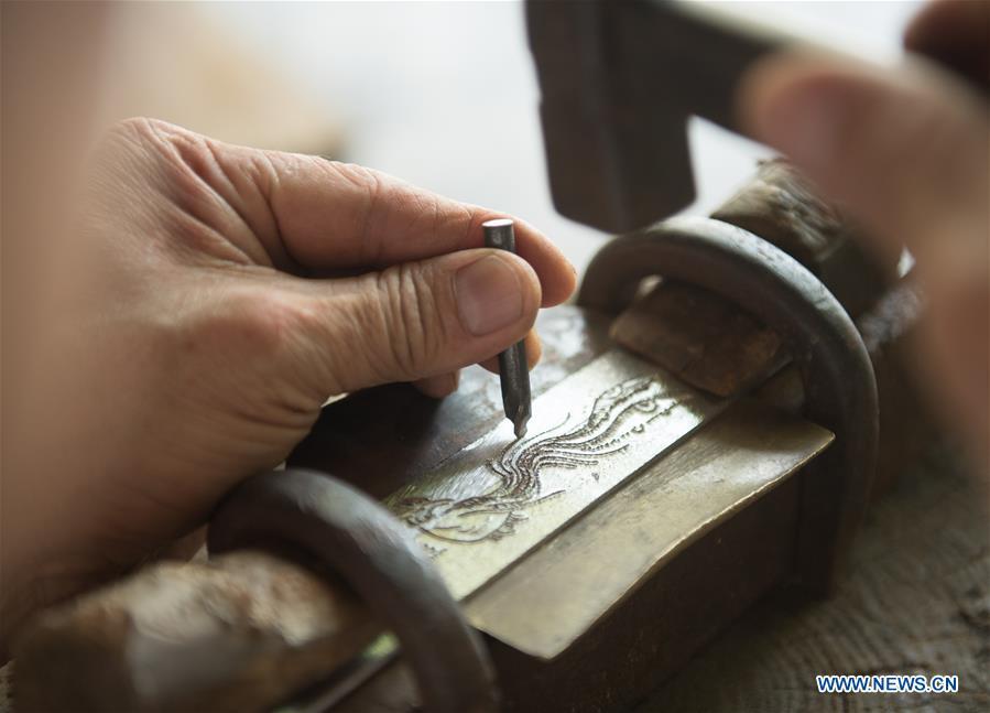 Zheng Guorong carves patten of a phoenix on a sword at Guyue Sword Studio in Longquan, east China\'s Zhejiang Province, May 21, 2019. For centuries, Longquan has been famed for its sword making industry. Zheng Guorong, 55, an intangible cultural heritage inheritor in Longquan Sword making, has been making sword for more than 30 years. Zheng regards sword as a symbol of spirit and devotes all to his career with awe. In his studio, the whole process of making a single sword takes two to three months, with steps including forming an idea, designing the sketch, preparing material and the final making and assembling. After setting up his studio, Zheng has trained more than 20 apprentices, who have all become sword smiths of great reputation. The old sword smith insists that Longquan sword, with a history of more than 2,500 years, deserves to be carried on in our time, both materially and spiritually. (Xinhua/Weng Xinyang)