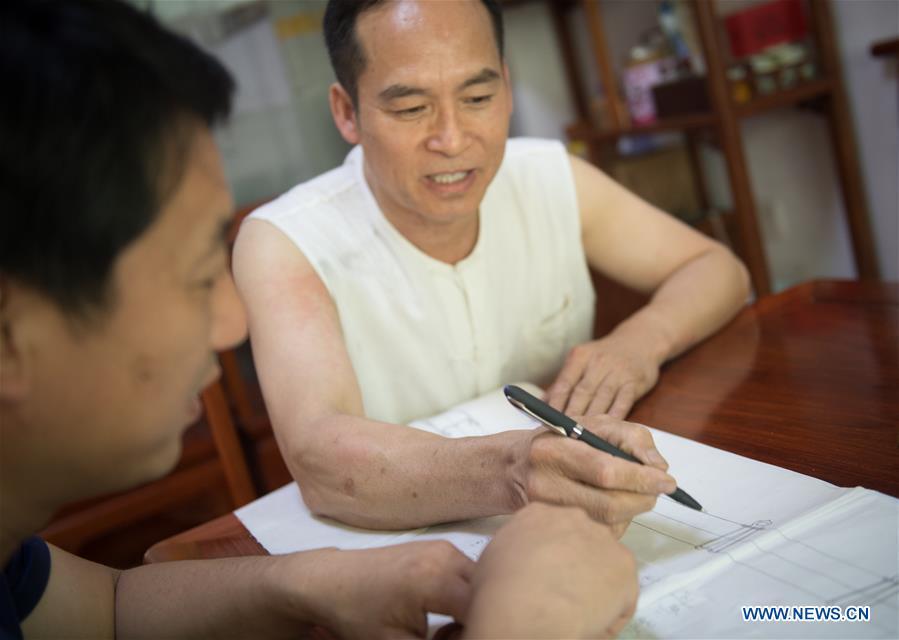 Zheng Guorong (R) discusses the design of sword with a customer at Guyue Sword Studio in Longquan, east China\'s Zhejiang Province, May 21, 2019. For centuries, Longquan has been famed for its sword making industry. Zheng Guorong, 55, an intangible cultural heritage inheritor in Longquan Sword making, has been making sword for more than 30 years. Zheng regards sword as a symbol of spirit and devotes all to his career with awe. In his studio, the whole process of making a single sword takes two to three months, with steps including forming an idea, designing the sketch, preparing material and the final making and assembling. After setting up his studio, Zheng has trained more than 20 apprentices, who have all become sword smiths of great reputation. The old sword smith insists that Longquan sword, with a history of more than 2,500 years, deserves to be carried on in our time, both materially and spiritually. (Xinhua/Weng Xinyang)