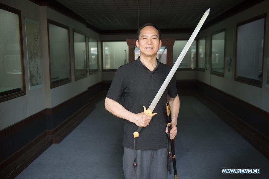 Zheng Guorong poses for a photo with a sword he made at Guyue Sword Studio in Longquan, east China\'s Zhejiang Province, May 21, 2019. For centuries, Longquan has been famed for its sword making industry. Zheng Guorong, 55, an intangible cultural heritage inheritor in Longquan Sword making, has been making sword for more than 30 years. Zheng regards sword as a symbol of spirit and devotes all to his career with awe. In his studio, the whole process of making a single sword takes two to three months, with steps including forming an idea, designing the sketch, preparing material and the final making and assembling. After setting up his studio, Zheng has trained more than 20 apprentices, who have all become sword smiths of great reputation. The old sword smith insists that Longquan sword, with a history of more than 2,500 years, deserves to be carried on in our time, both materially and spiritually. (Xinhua/Weng Xinyang)
