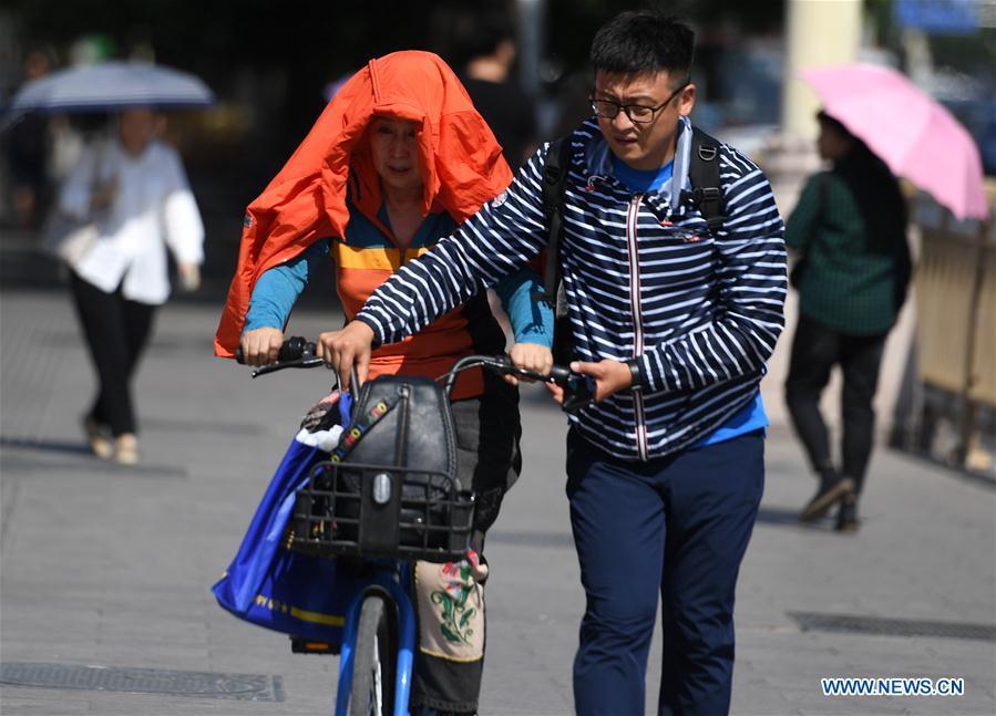 A pedestrian (L) puts a jacket over her head and shoulders as sun shade in Beijing, capital of China, May 22, 2019. Beijing\'s observatory issued a yellow alert on Tuesday for high temperatures over the next four days. Temperature could rise to 35 degrees Celsius from Wednesday to Saturday, and reach up to 37 degrees Celsius on Thursday. (Xinhua/Zhang Chenlin)