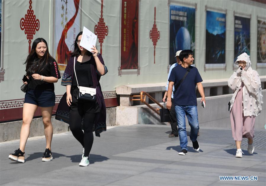 A pedestrian (2nd L) uses a personal item as sun shade in Beijing, capital of China, Beijing\'s observatory issued a yellow alert on Tuesday for high temperatures over the next four days. Temperature could rise to 35 degrees Celsius from Wednesday to Saturday, and reach up to 37 degrees Celsius on Thursday. (Xinhua/Zhang Chenlin)
