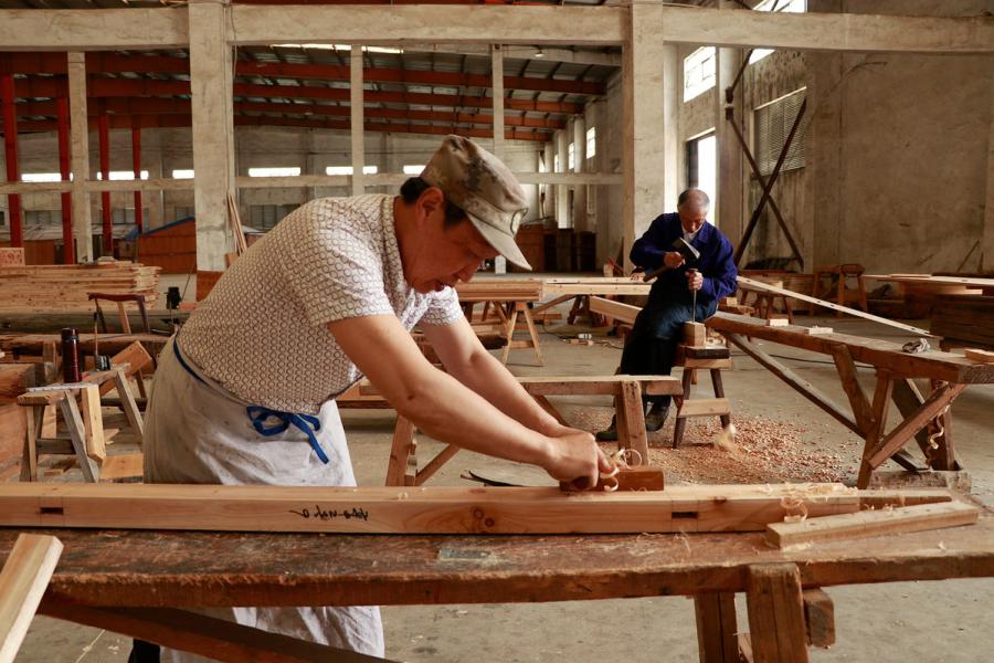Two carpenters work on new wooden components for repairing ancient residences in the warehouse of Bengbu Ancient Residence Exhibition Park, based in Bengbu city of East China\'s Anhui province. （By Zhu Lixin/chinadaily.com.cn）