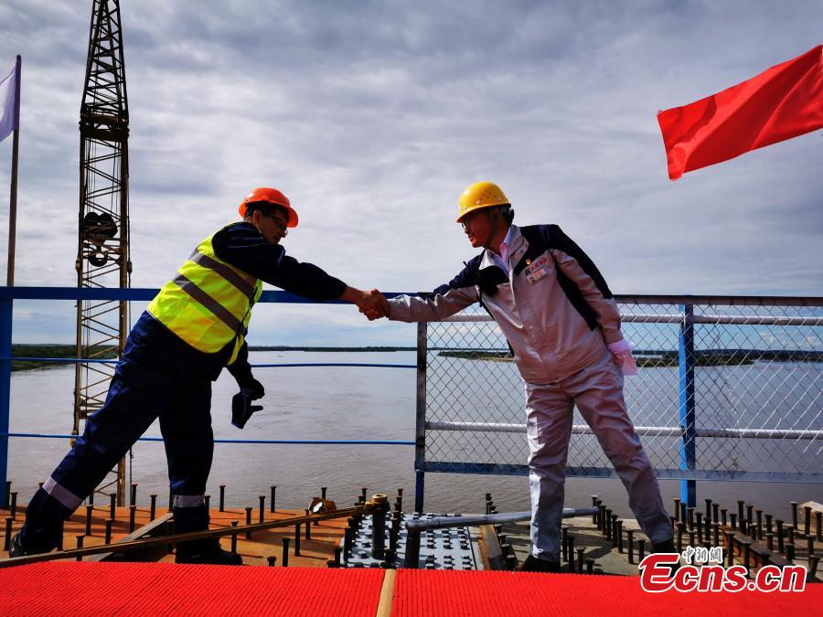 Construction workers from China and Russia shake hands after putting in the last bolts to connect the highway bridge across the Heilongjiang River, called the Amur River in Russia.  (Photo: China News Service/Shao Guoliang)