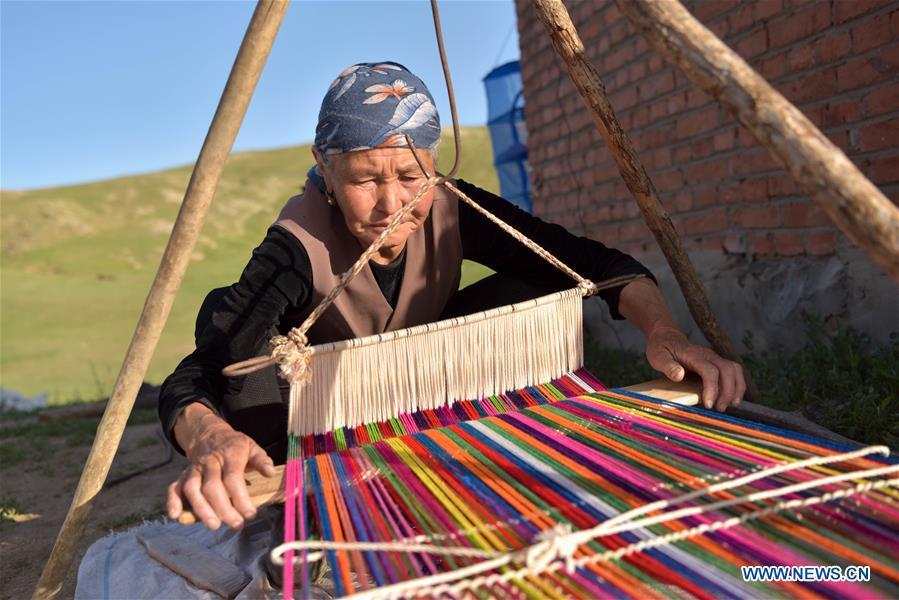 A herdswoman is seen weaving in a pasturing area at Fuhai County of Altay, northwest China\'s Xinjiang Uygur Autonomous Region, on June 5, 2019. As summer comes, herdsmen of Kazak ethnic group here are busy with transferring livestock to summer pastures. (Xinhua/Ding Lei)