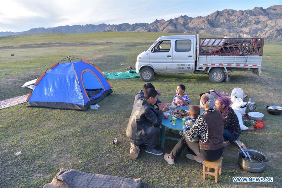 People have dinner during their transfer to summer pasture in Fuhai County of Altay, northwest China\'s Xinjiang Uygur Autonomous Region, on June 5, 2019. As summer comes, herdsmen of Kazak ethnic group here are busy with transferring livestock to summer pastures. (Xinhua/Ding Lei)