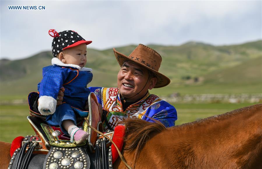 A herdsman puts his son on the horseback during the nomadic migration on the Ar Horqin grassland in Chifeng City, north China\'s Inner Mongolia Autonomous Region, May 31, 2019. Yearly nomadic grazing is still a tradition for people live on the Ar Horqin grassland, where was listed of National Important Agricultural Heritage Systems in 2014. For a long time, herdsmen would decide the route and time of yearly nomadic grazing according to the growth of grassland. (Xinhua/Peng Yuan)