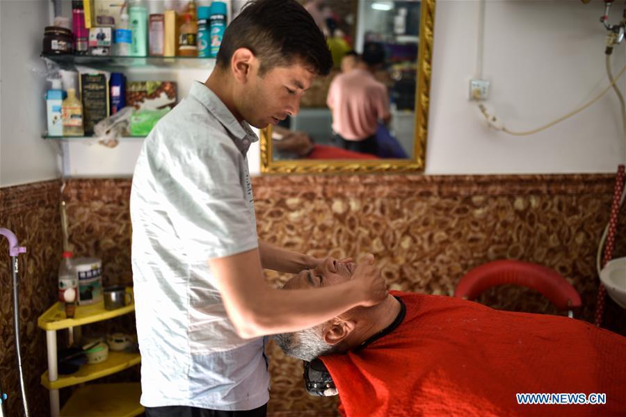 A barber provides shaving service for a local resident in the ancient city of Kashgar, northwest China\'s Xinjiang Uygur Autonomous Region, June 12, 2019. The ancient city of Kashgar has been well prepared for the peak tourism season through multiple measures including improving infrastructure and service quality as well as staging acrobatics performances to help tourists better experience the time-honored folk culture here. (Xinhua/Zhao Ge)