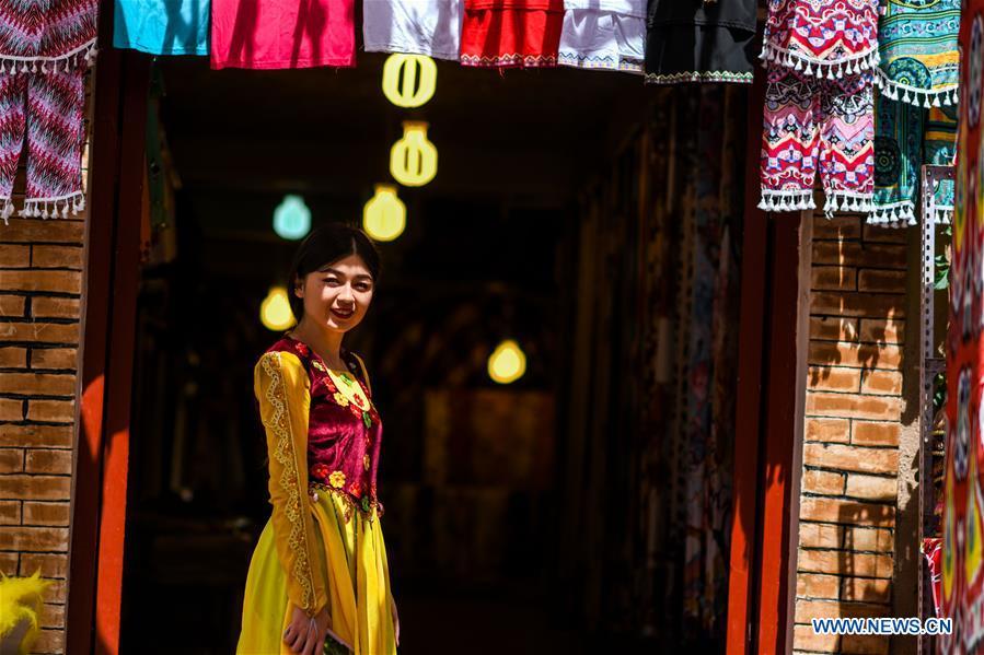 A staff member poses for a photo outside a shop in the ancient city of Kashgar, northwest China\'s Xinjiang Uygur Autonomous Region, June 12, 2019. The ancient city of Kashgar has been well prepared for the peak tourism season through multiple measures including improving infrastructure and service quality as well as staging acrobatics performances to help tourists better experience the time-honored folk culture here. (Xinhua/Zhao Ge)