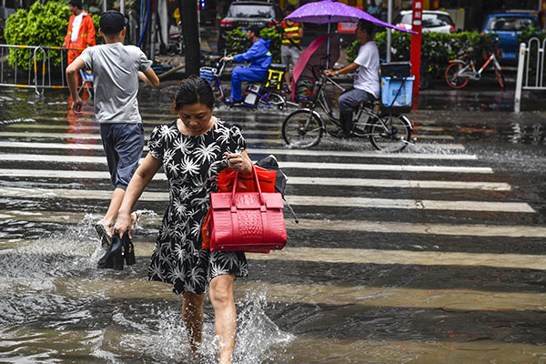 People walk across a flooded street in Guangzhou, Guangdong province, on Monday. Kindergartens and primary and middle schools were closed after Typhoon Mawar battered the city.(Photo/Chinanews.com) People walk across a flooded street in Guangzhou, Guangdong province, on Monday. Kindergartens and primary and middle schools were closed after Typhoon Mawar battered the city.(Photo/Chinanews.com)