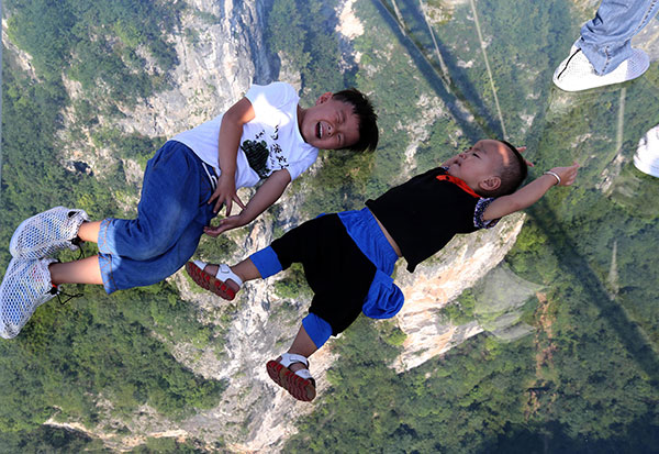 Children lie down on the glass-bottom bridge in Zhangjiajie, Hunan province, on Saturday. It is said to be the world's highest and longest glass-bottom bridge. (Photo by Zhou Guoqiang/China Daily) 